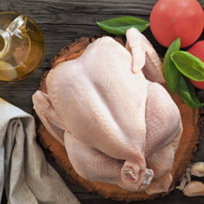 Premium whole chicken skin on a wooden cutting board with olive oil, tomatoes, and garlic.