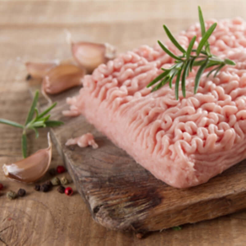 Premium chicken mince on a wooden board with garlic and herbs, perfect for cooking delicious dishes.